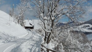 A snow-covered rural road with a wooden fence and a building in the background.