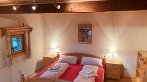 A bedroom with a wooden bed, two bedside tables with lamps, a small window with curtains, and a painting on the wall.