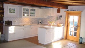 A kitchen with white cabinets, a wooden ceiling, and a door leading outside.