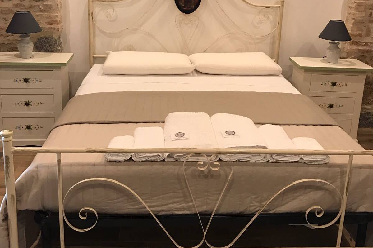 Een slaapkamer met een bed, twee nachtkastjes, een lamp op elk kastje, en een bakstenen muur.