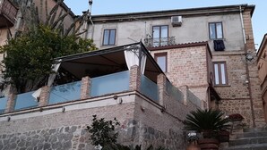 A stone building with a staircase, potted plants, and a car parked in front.