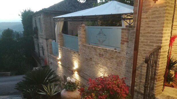 A rustic building with a brick facade, a white awning, and a stone planter with red flowers.