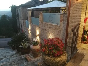 A rustic building with a brick facade, a white awning, and a stone planter with red flowers.