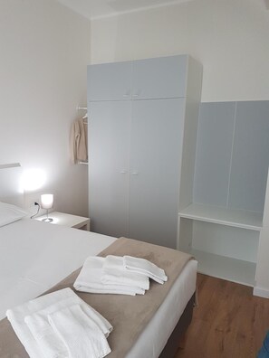 A bedroom with a bed, a nightstand, a wardrobe, and a shelf unit.
