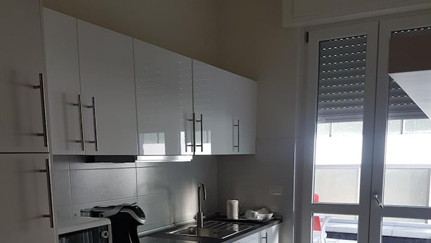 A modern kitchen with white cabinets, a black countertop, and a built-in microwave. - Affittacamere Risorgimento (Lecco)