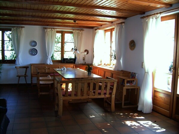 A wooden dining area with a table and chairs, a hanging light, and a window with curtains. - Cozy, comfortable country house in a dream location (Templin)