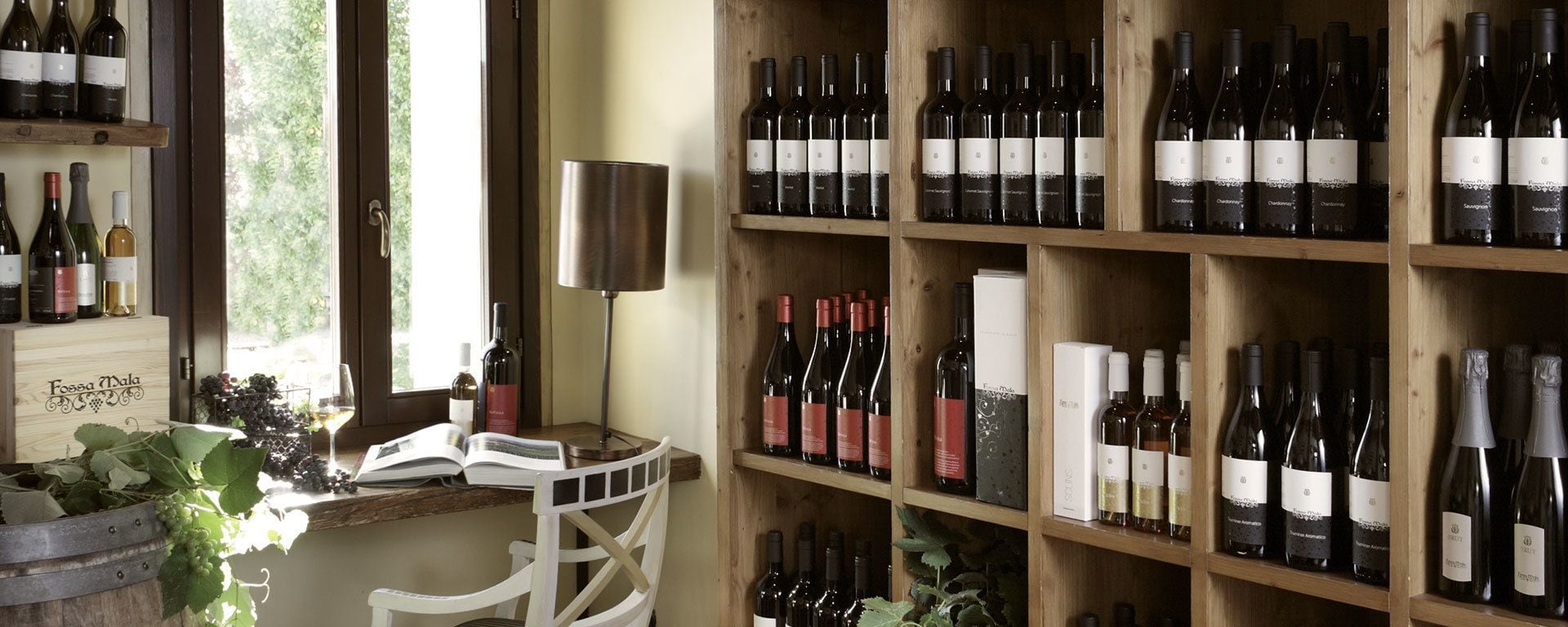 A wine cellar with wooden shelves filled with various wine bottles, a wine rack, and a table with a book and a wine glass.