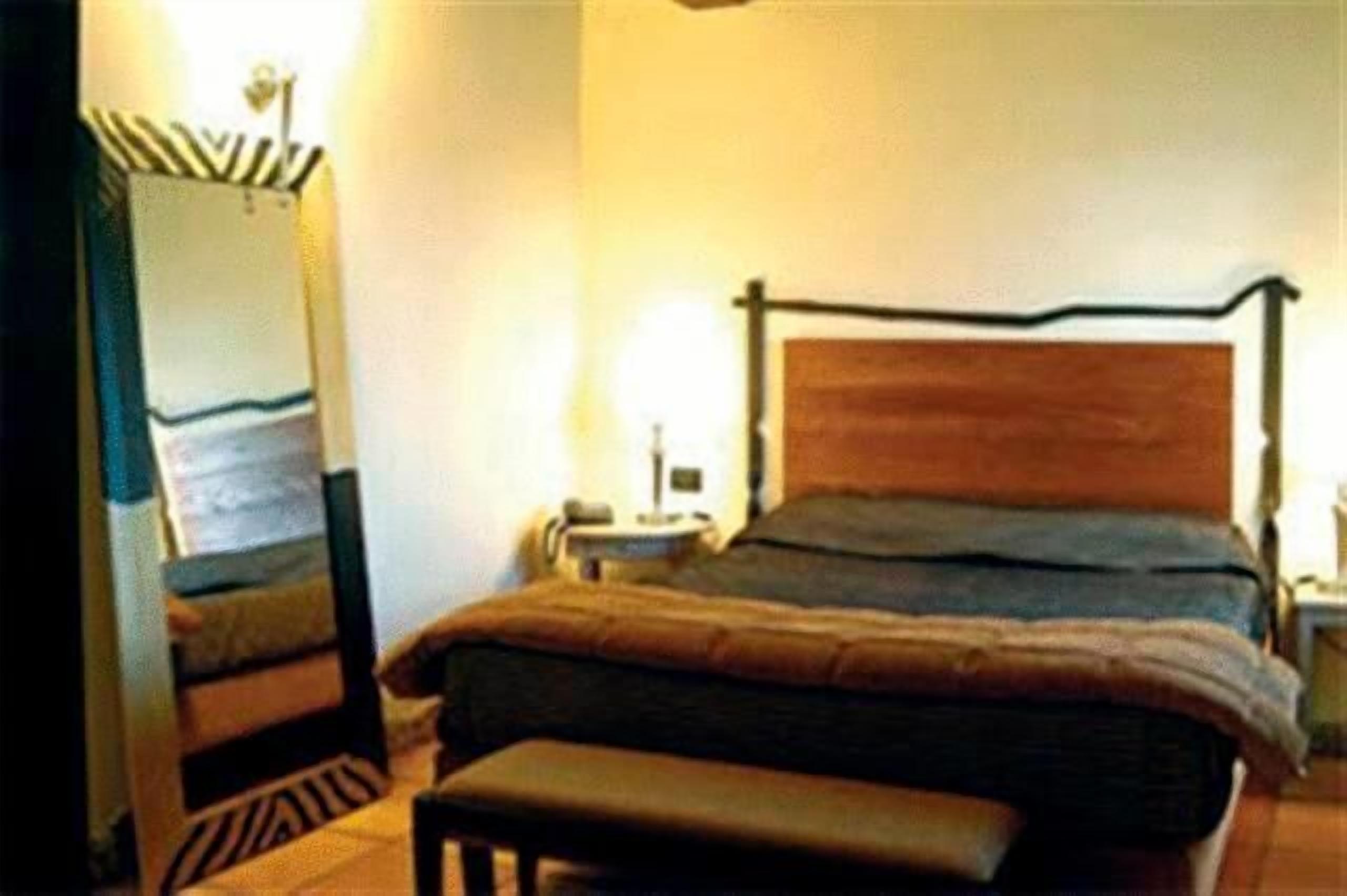 A bedroom with a wooden bed, a nightstand, a lamp, and a mirror.