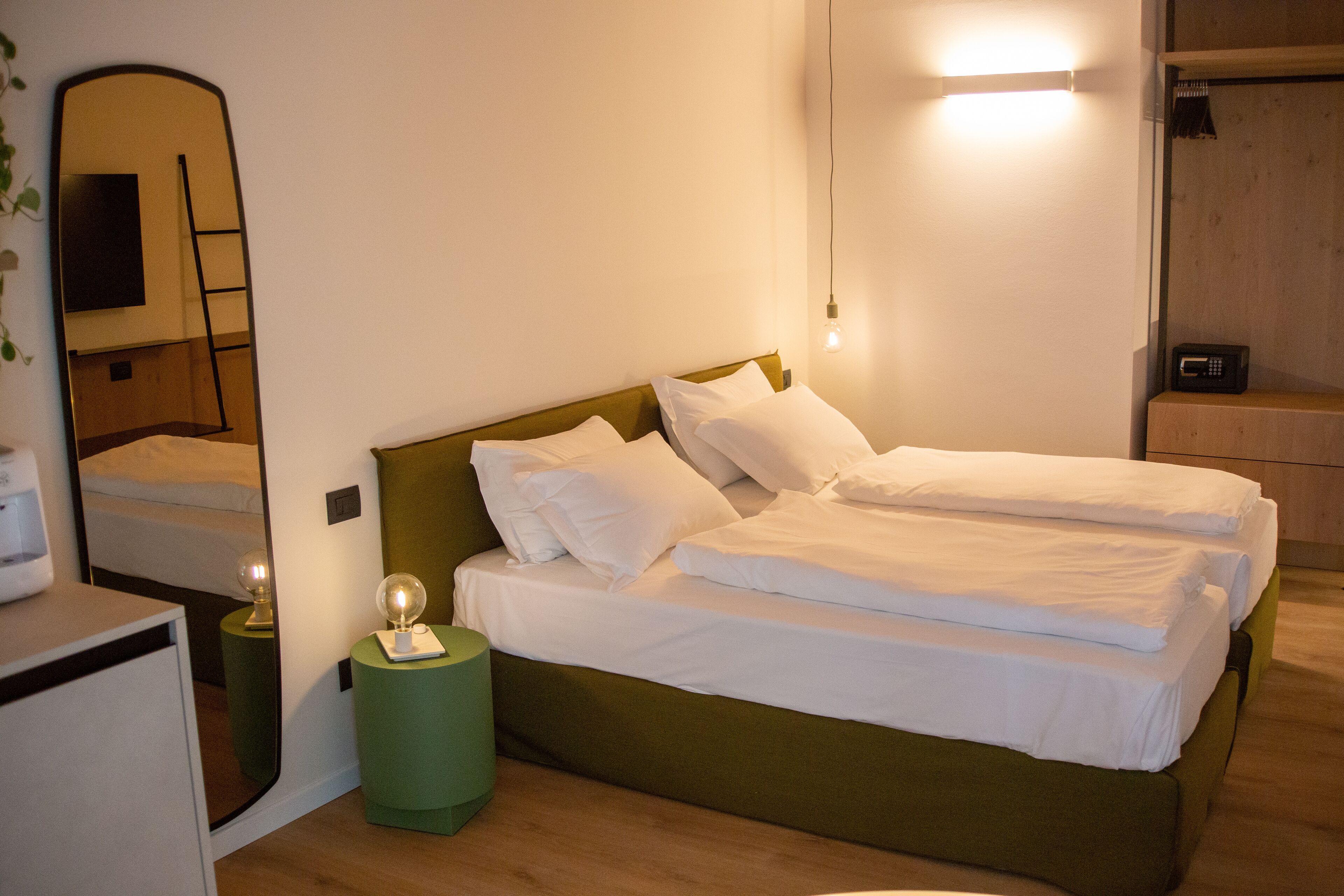Una cama individual con ropa blanca de cama, cabecera verde y mesita de noche con lámpara.