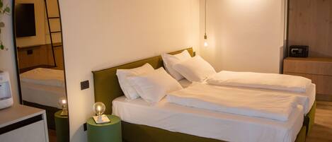 Una cama individual con ropa blanca de cama, cabecera verde y mesita de noche con lámpara.