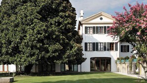 Un bâtiment blanc à deux étages, avec un grand arbre dans le jardin.