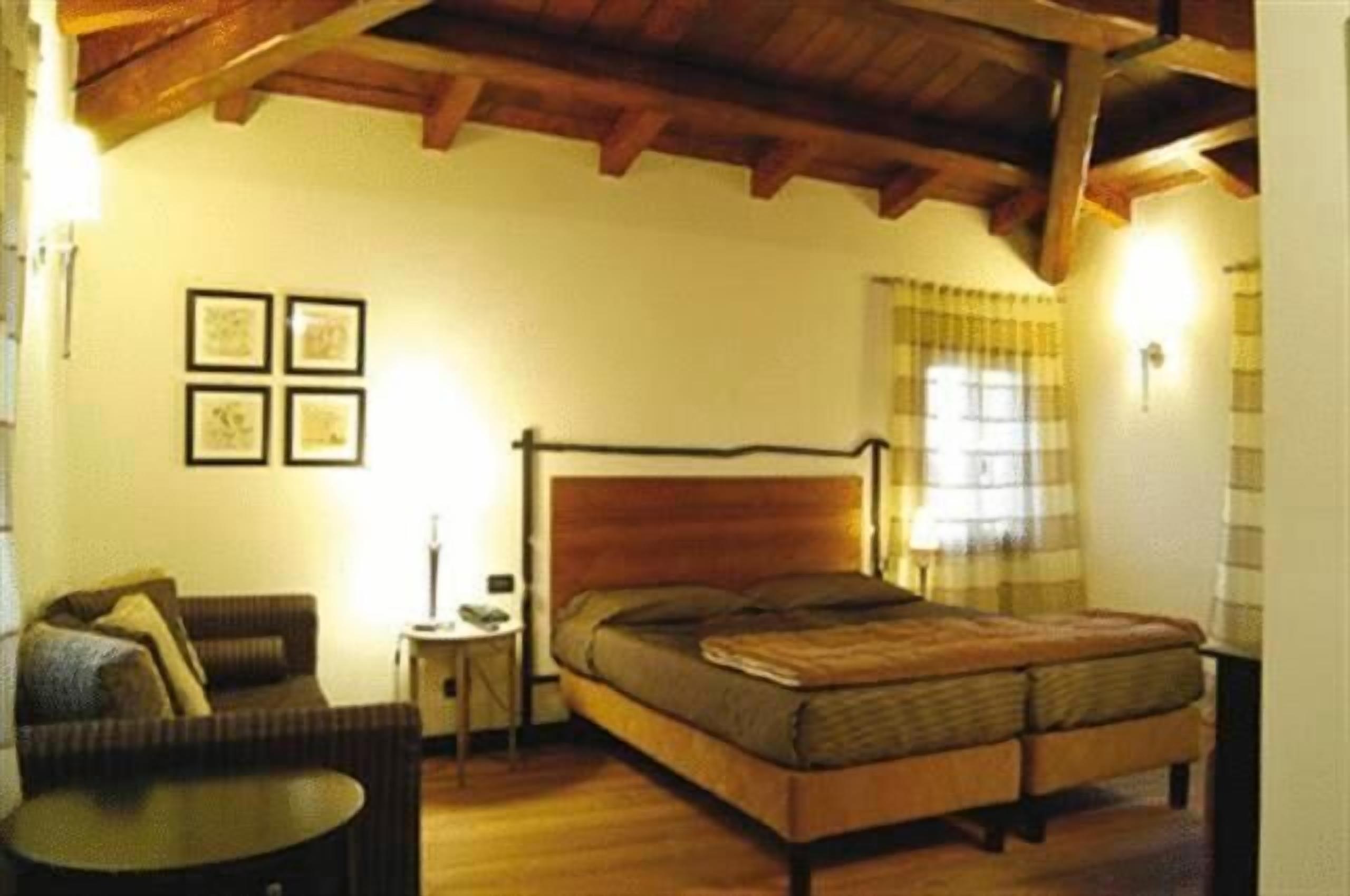 Un dormitorio con una cama de madera, una mesita redonda pequeña, un sofá y una pared decorada con marcos.