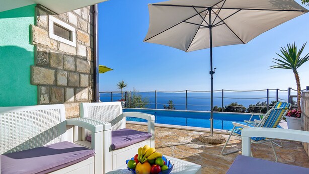 Ein Poolbereich mit Meerblick, einem Tisch mit Obst und Liegestühlen.
