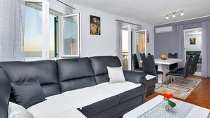 Ein modernes Wohnzimmer mit einer schwarzen Ledersofa, einem Essbereich mit weißem Tisch und Stühlen und Blick ins Freie.