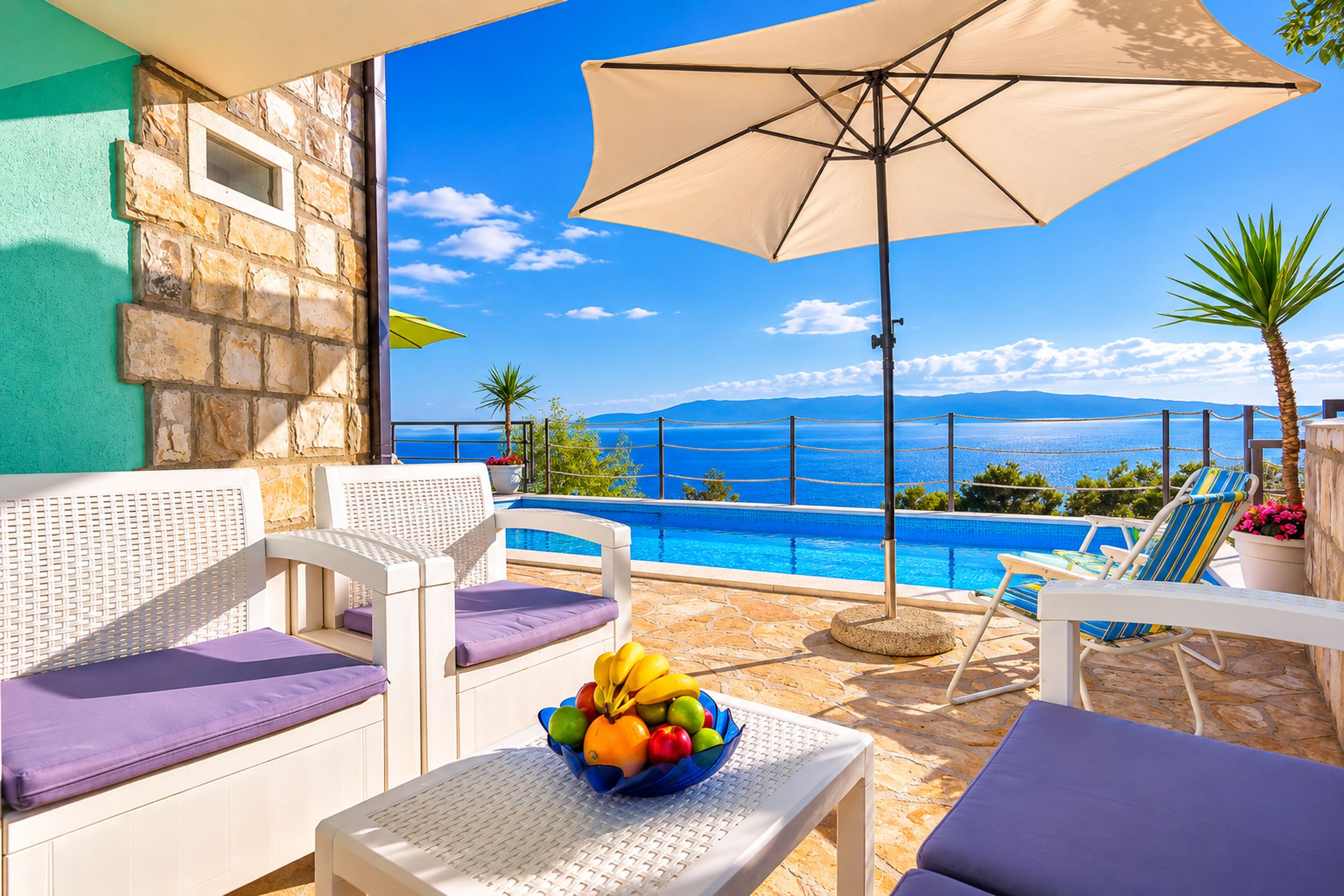 A poolside area with lounge chairs, a table with fruit, and a view of the sea.