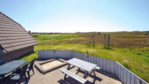 Un patio con una mesa y sillas, un conjunto de columpios de madera y vistas a un campo cubierto de césped.
