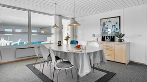 Un comedor moderno con una mesa redonda, sillas, lámparas colgantes, vistas a una piscina y una zona de cocina con armarios y una obra de arte enmarcada.