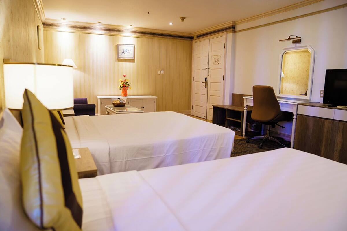 Une chambre d’hôtel avec deux lits, un bureau, une chaise, une télévision et une armoire.