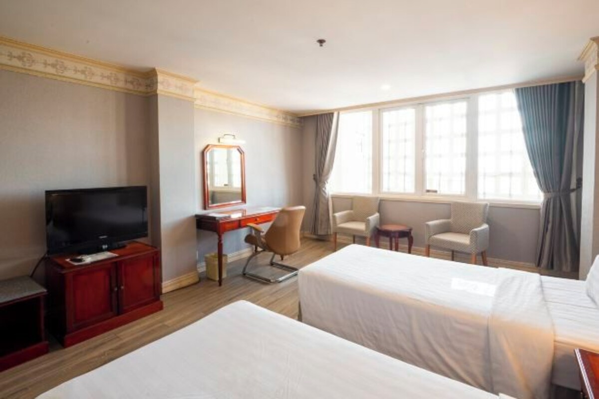Habitación de hotel con dos camas, televisión, escritorio con silla y ventana con cortinas.