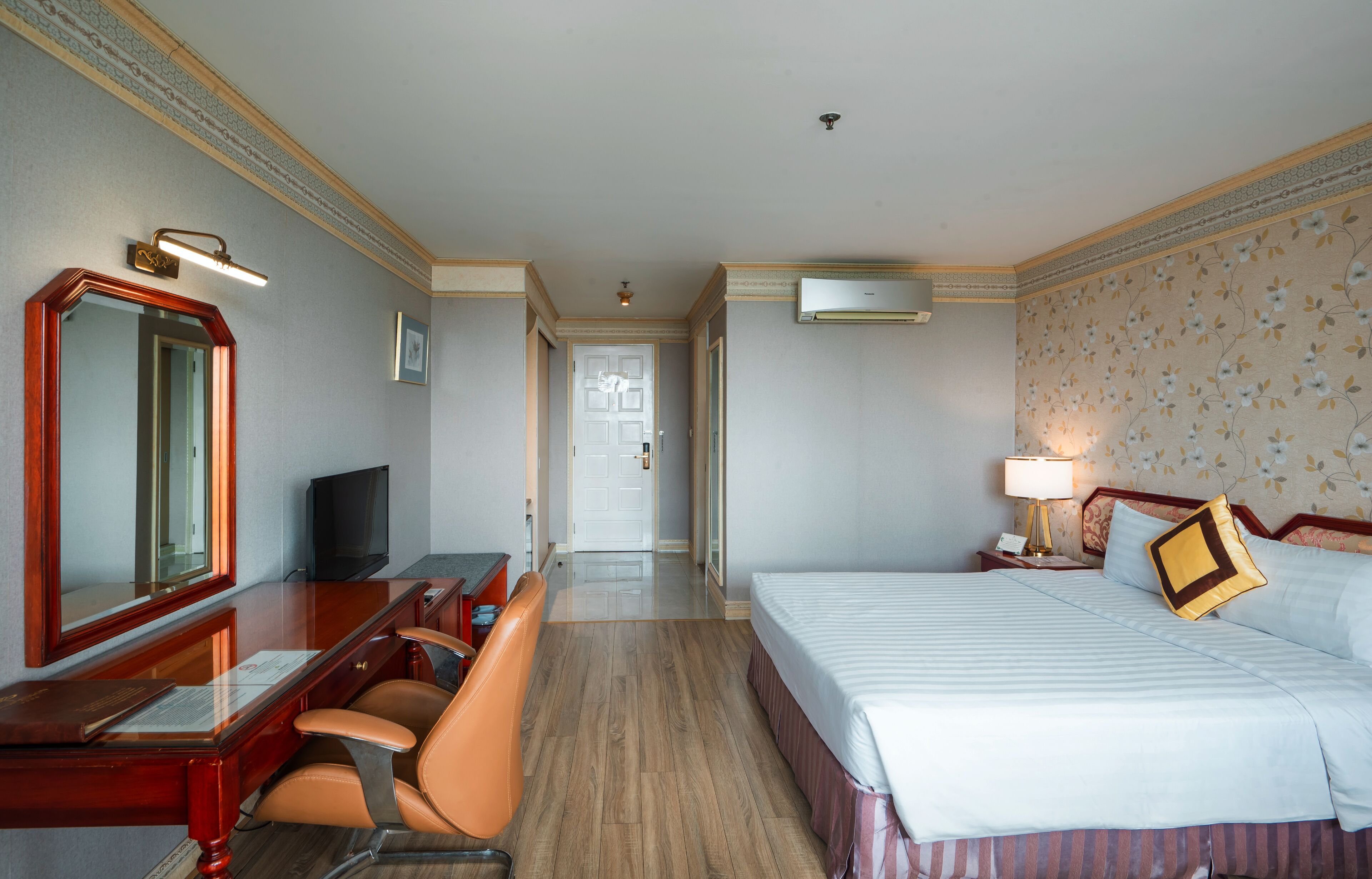 A hotel room with a bed, a desk with a chair, a television, and a mirror.
