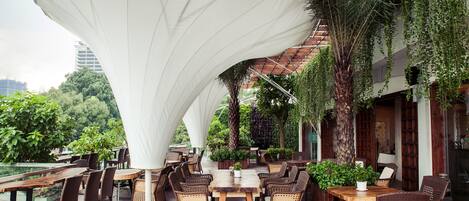 An outdoor patio with wicker furniture, white canopies, and lush greenery.