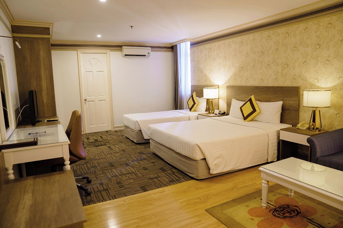 A hotel room with two beds, a desk, a chair, a sofa, and a television.