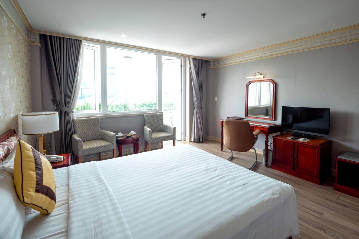 Une chambre d’hôtel avec un grand lit, deux fauteuils, un bureau avec une télévision et une fenêtre avec des rideaux.