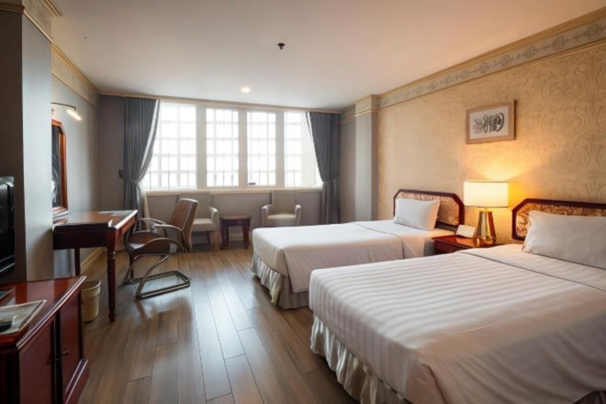A hotel room with two beds, a desk, a chair, a TV, and a window with curtains.