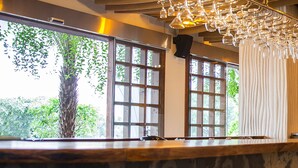 Zona de bar con techo de madera, ventanas amplias y lámparas colgantes.