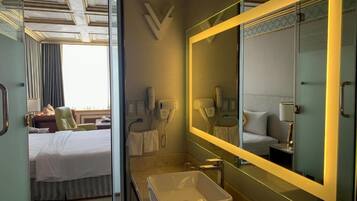 A hotel room with a bed, a bathroom with a large mirror, a sink, and a shower.