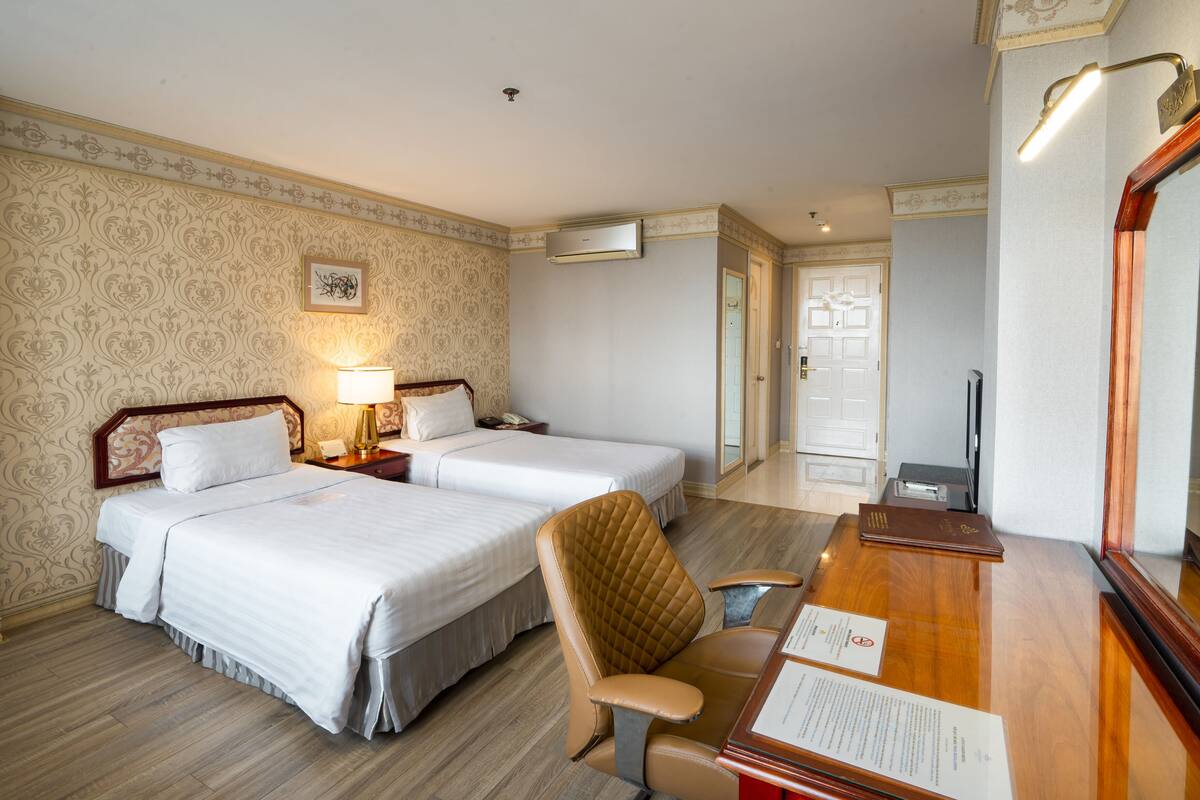 Une chambre d’hôtel avec deux lits, un bureau, une chaise, une lampe, un miroir et une porte.
