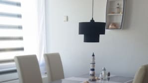 Uma sala de jantar com uma mesa branca e quatro cadeiras. Um pequeno modelo de navio está sobre a mesa.