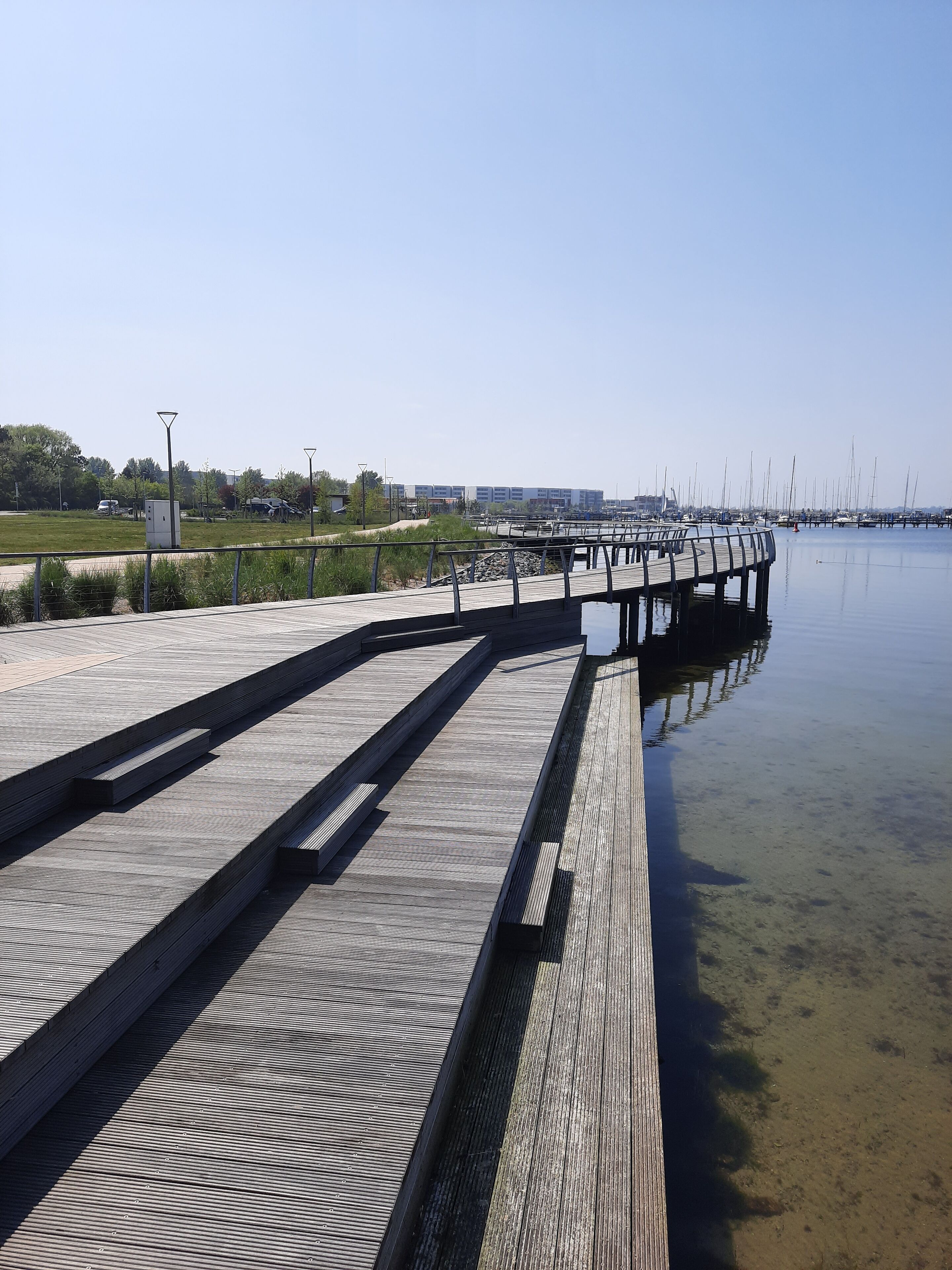 Een houten looppad strekt zich uit over kalm water, met een heldere lucht erboven.