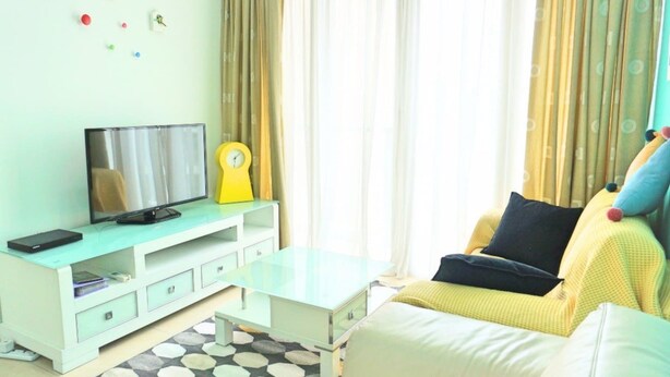 A living room with a TV, a yellow clock, a sofa, and a coffee table. - Marc A-30-06 by SYNC (Kuala Lumpur)