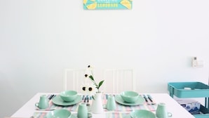 A dining table set with teal-colored dishes and a white pitcher, a wall-mounted sign with text, and a white radiator. - Marc A-30-06 by SYNC (Kuala Lumpur)