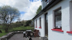 Un mur de pierre, un chemin de gravier, un chien et un bâtiment avec des fenêtres et des bordures rouges.
