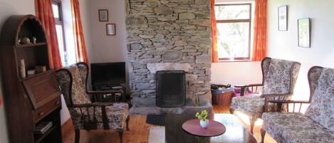 A cozy living room with a stone fireplace, wooden furniture, and a television.