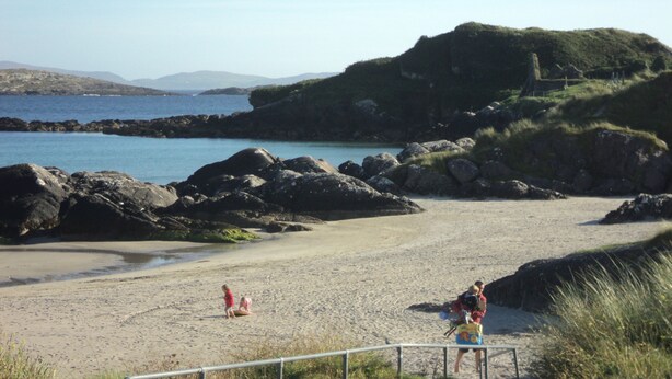 Une plage avec des formations rocheuses et, en arrière-plan, une colline couverte d’herbe.