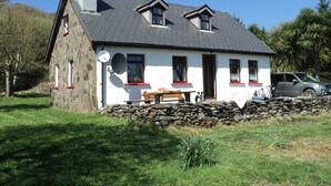 Une maison en pierre avec un toit en pente, une cheminée et un mur de pierre à l’avant.