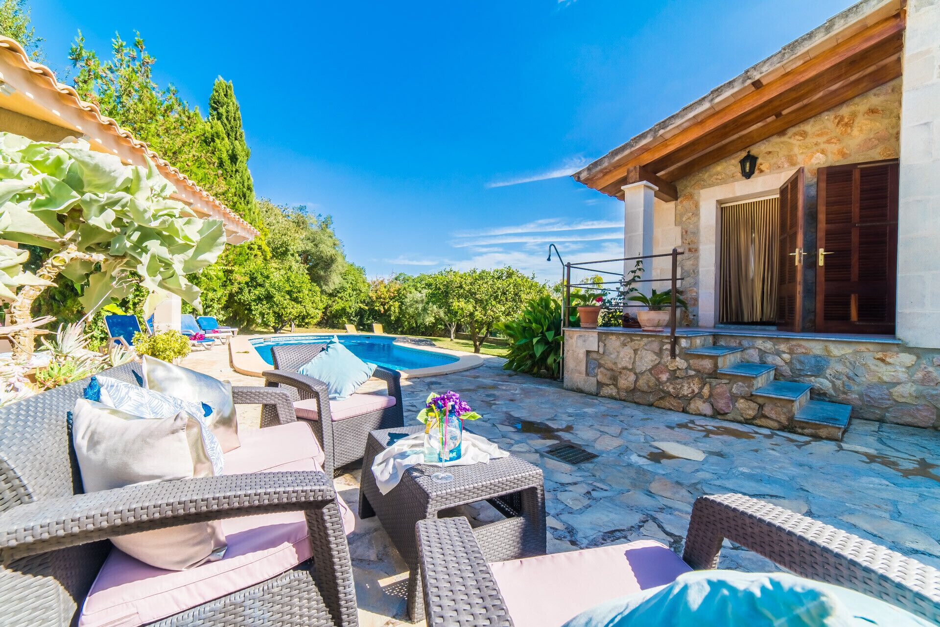 A poolside area with wicker furniture, a stone building, and a clear blue sky.