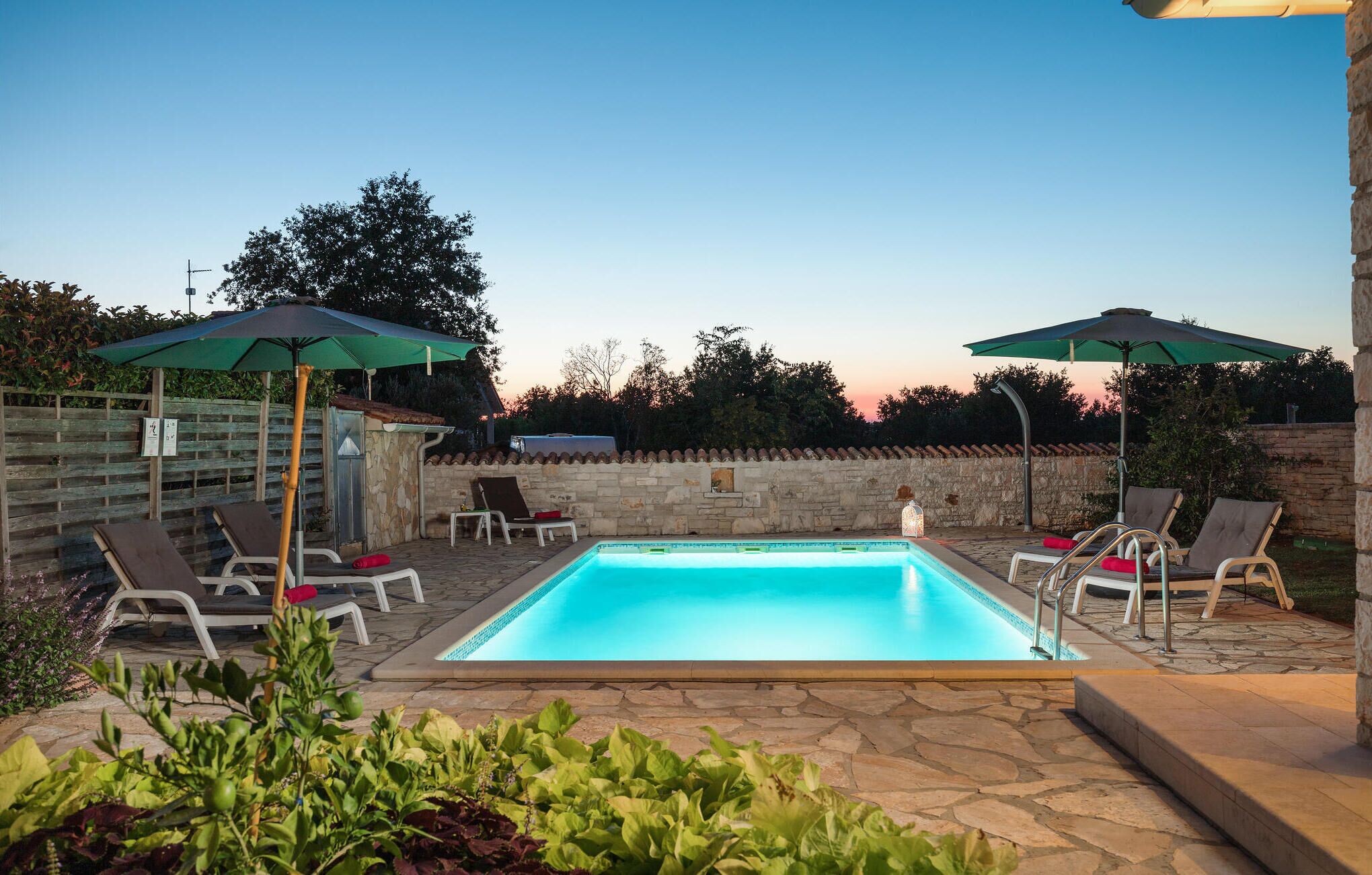 A rectangular swimming pool with lounge chairs and umbrellas, surrounded by stone walls and greenery.