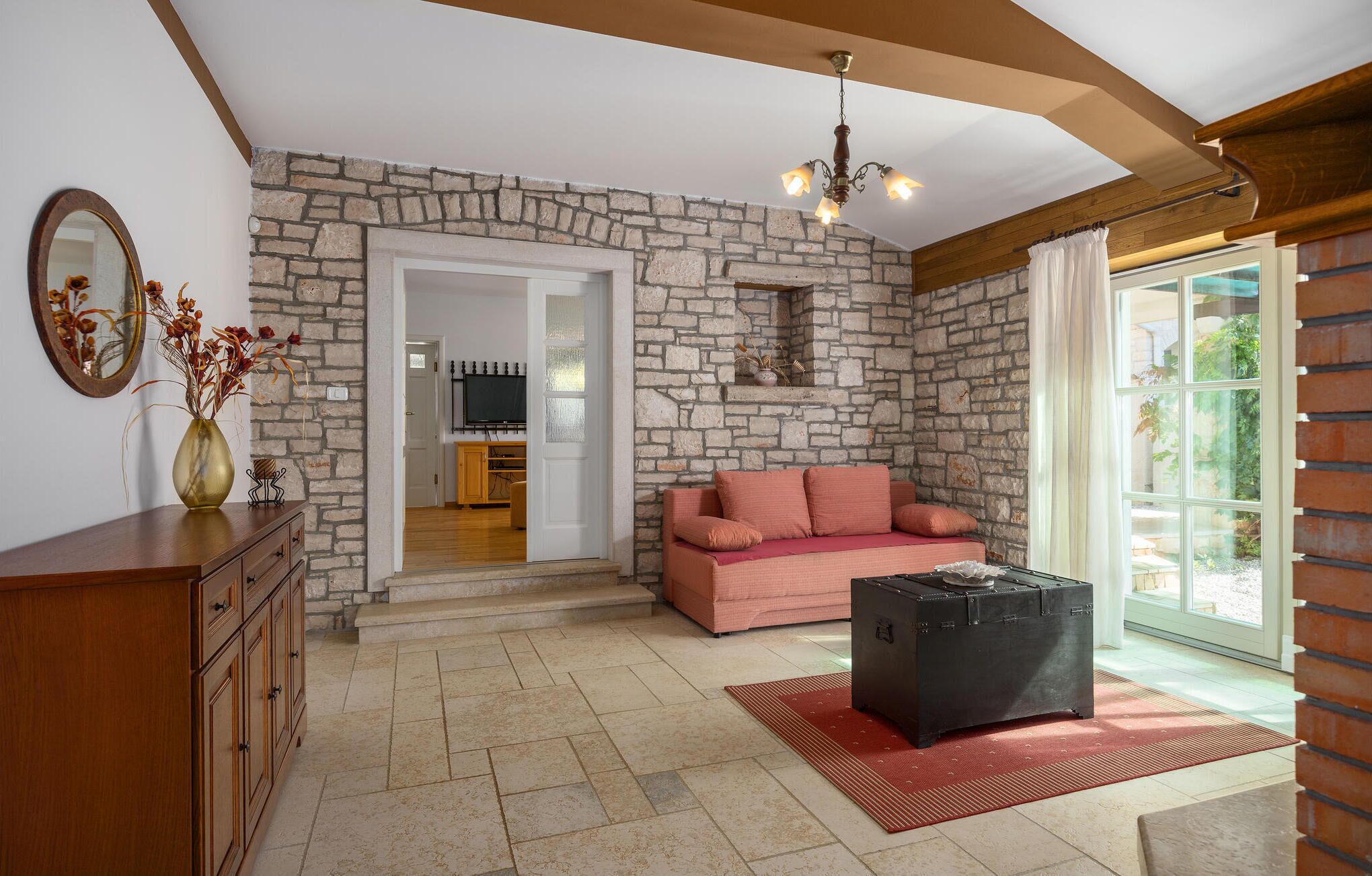 A cozy living room with a stone wall, a pink sofa, a wooden cabinet, and a black storage box.