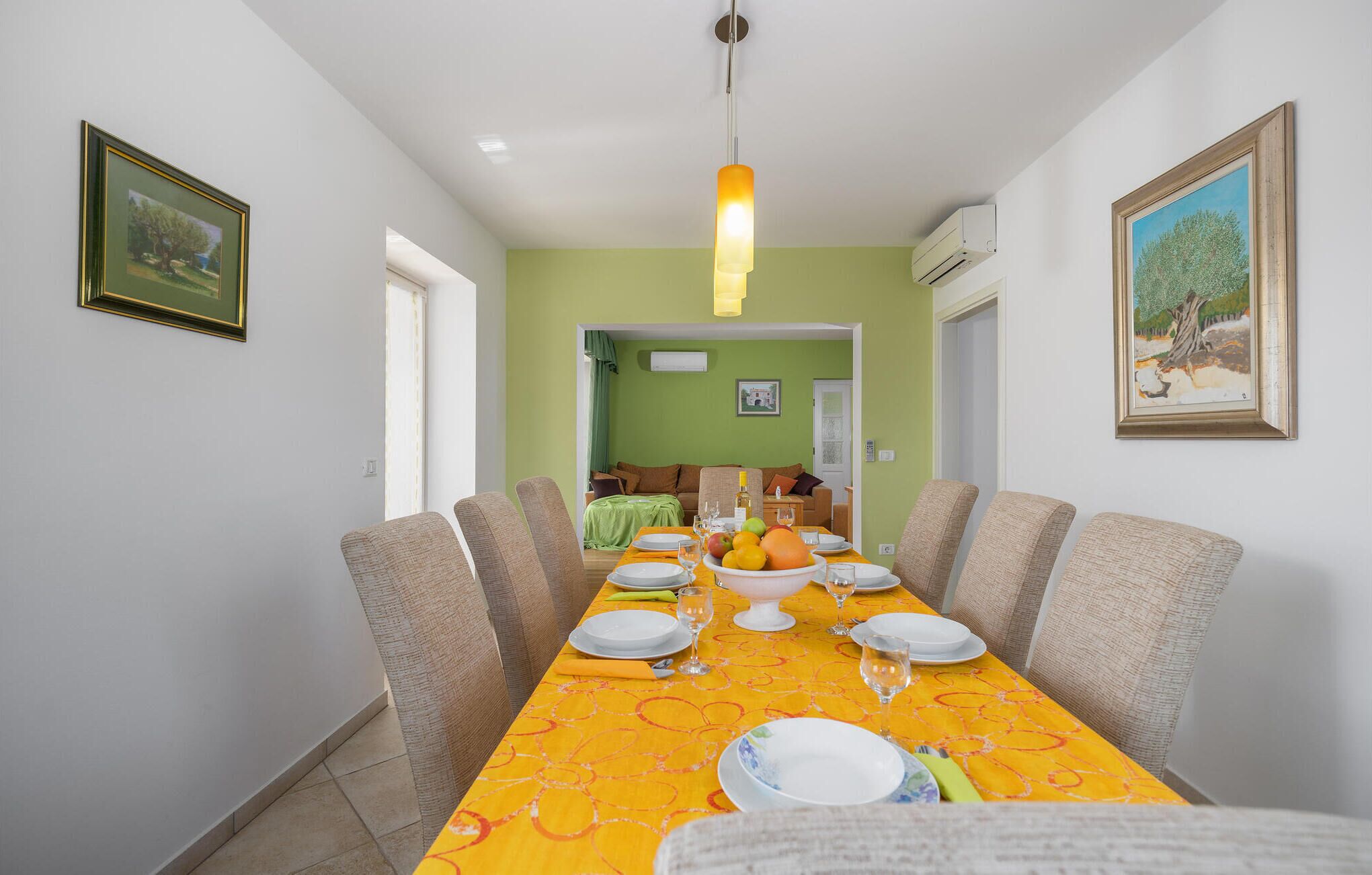 A dining area with a long table set for six, surrounded by six chairs. There is a hanging light fixture above the table.