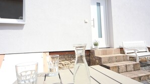Une terrasse avec une table, deux verres, une carafe d’eau et un banc blanc.