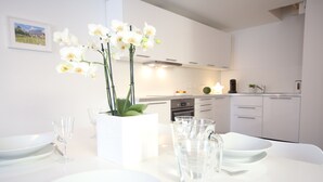 Une cuisine moderne avec des meubles blancs, une table à manger dressée avec des assiettes et des verres, et un vase rempli de fleurs blanches.