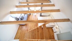 Une pièce aux hauts plafonds, avec des poutres apparentes en bois, un plancher en bois, un mur blanc, une fenêtre et une baignoire blanche.