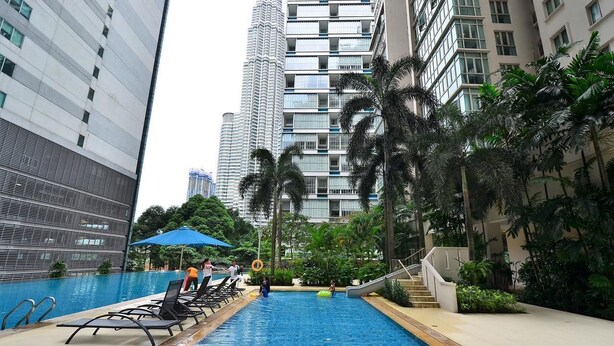 A swimming pool with lounge chairs, palm trees, and high-rise buildings in the background. - Marc A-23-09 by SYNC (Kuala Lumpur)