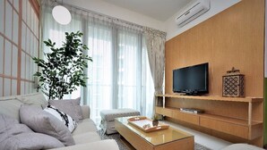 A modern living room with a sofa, a coffee table, a TV on a wooden wall, and a large plant. - Marc A-23-09 by SYNC (Kuala Lumpur)