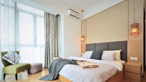A modern hotel room with a large bed, a seating area with a chair and ottoman, a bedside table, and a large window with curtains. - Marc A-23-09 by SYNC (Kuala Lumpur)