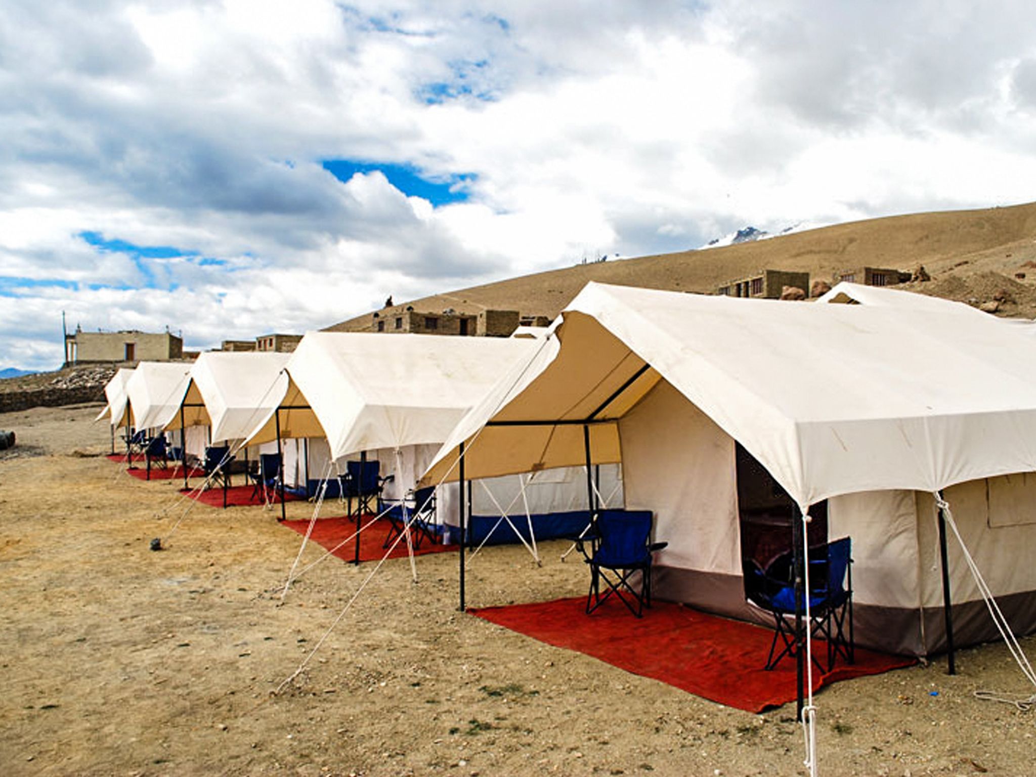 A row of tents with red carpets and blue chairs, set in a desert landscape with a clear sky.